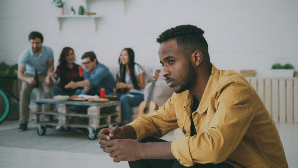 Person sitting apart from a group while wondering why do I feel lonely around people.