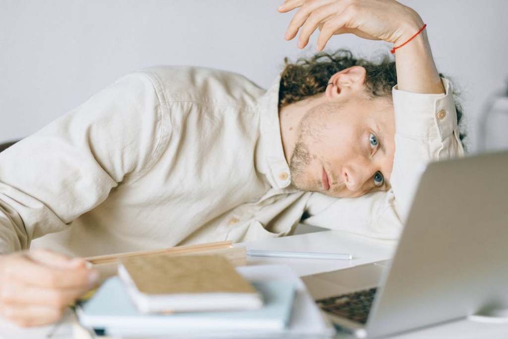 Tired person lying beside a laptop while wondering am i burned out or lazy after losing motivation.